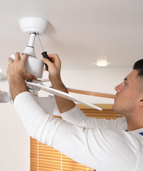 Electrician with screwdriver repairing ceiling fan indoors
